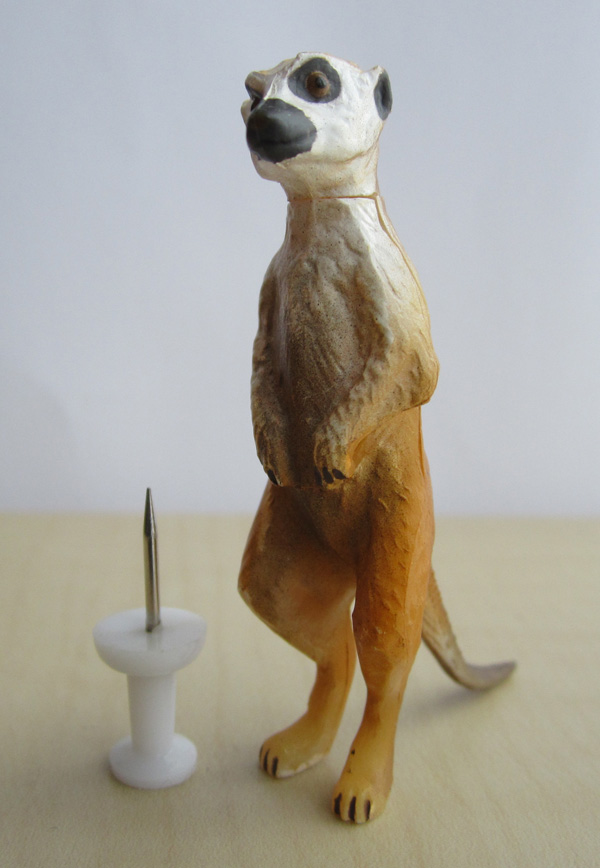 A meerkat miniature figurine, standing up on its hind legs. A pin shows that the figure is about 6 cm high. 